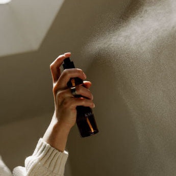Hand holding a black spray bottle against a neutral background

